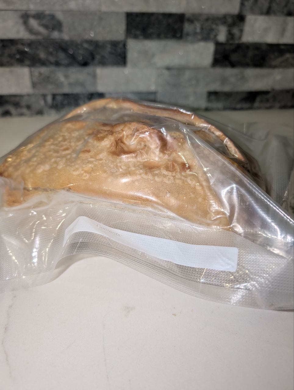 A whole sourdough loaf vacuum sealed in a clear bag on a countertop